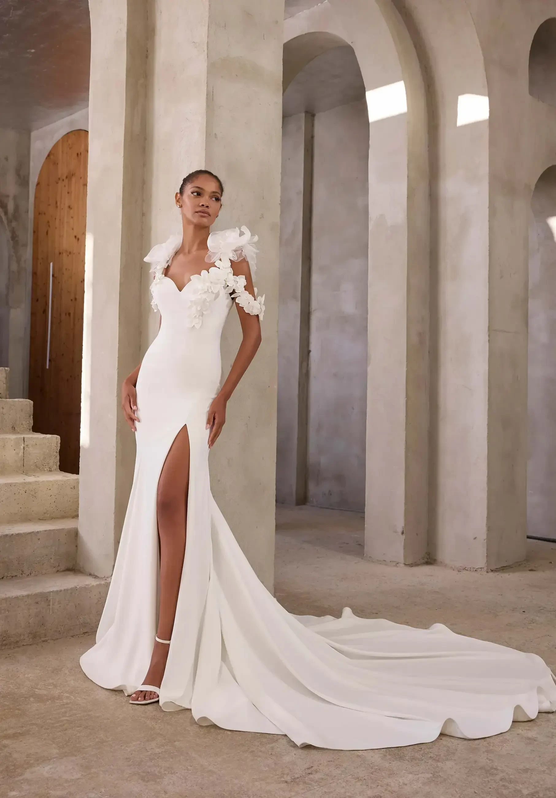 model is wearing a cold shoulder wedding dress with a high slit and lace details
