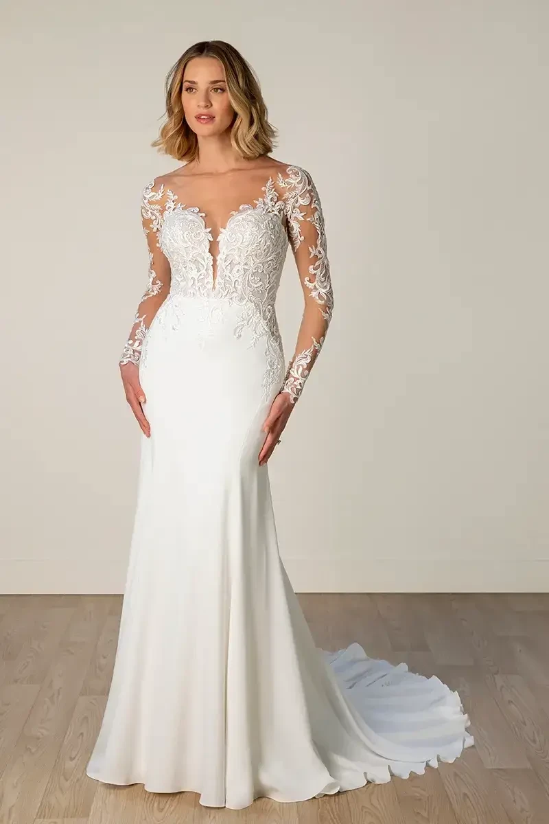 Model is wearing a lace fit-and-flare gown with a high illusion neckline, sheer long lace sleeves, a low open back, and a sleek trumpet skirt.
