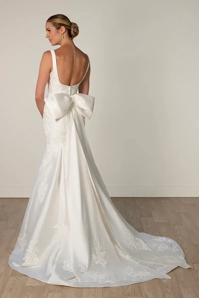 Model is wearing a Mikado fit-and-flare gown with a square neckline, low scoop back, detachable oversized bow, and optional lace accents.